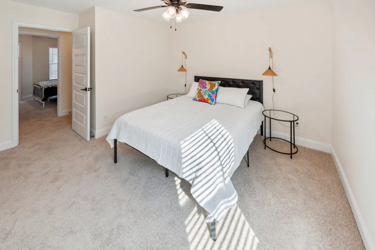 This image captures a tranquil bedroom with a plush bed adorned with a colorful pillow, decorative wall lamps, and a window letting in soft natural light. The overall ambiance is peaceful and serene, ideal for unwinding and privacy.