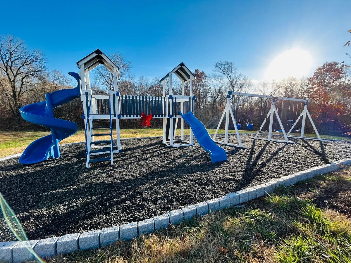 This image features an exterior view of a playground area, with a prominent playground structure, swings, and a slide. The space is vibrant, full of natural light, and invites outdoor activities, suggesting a family-friendly neighborhood environment.