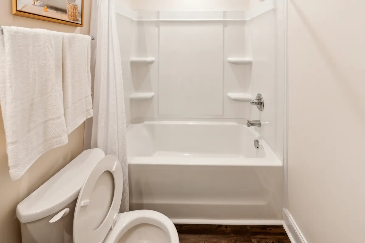 A calm, well-appointed full bathroom featuring a bathtub, toilet, towels, and tasteful wall art. The setting invites relaxation and self-care routines, offering a refreshing break at any time of day.