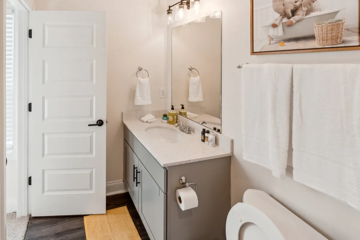 This image features a serene bathroom with a vanity, sink, mirror, artwork, and neatly arranged towels. The ambiance is calm and inviting, emphasizing thoughtful amenities and personal care spaces.