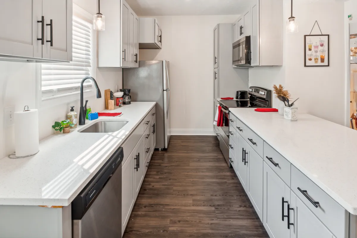 A modern kitchen featuring a spacious island, sleek stainless steel appliances, a large sink, and a window with blinds that allows natural light to stream in. The layout highlights ample counter space, with contemporary cabinetry and a welcoming, functional atmosphere ideal for both everyday use and entertaining guests.