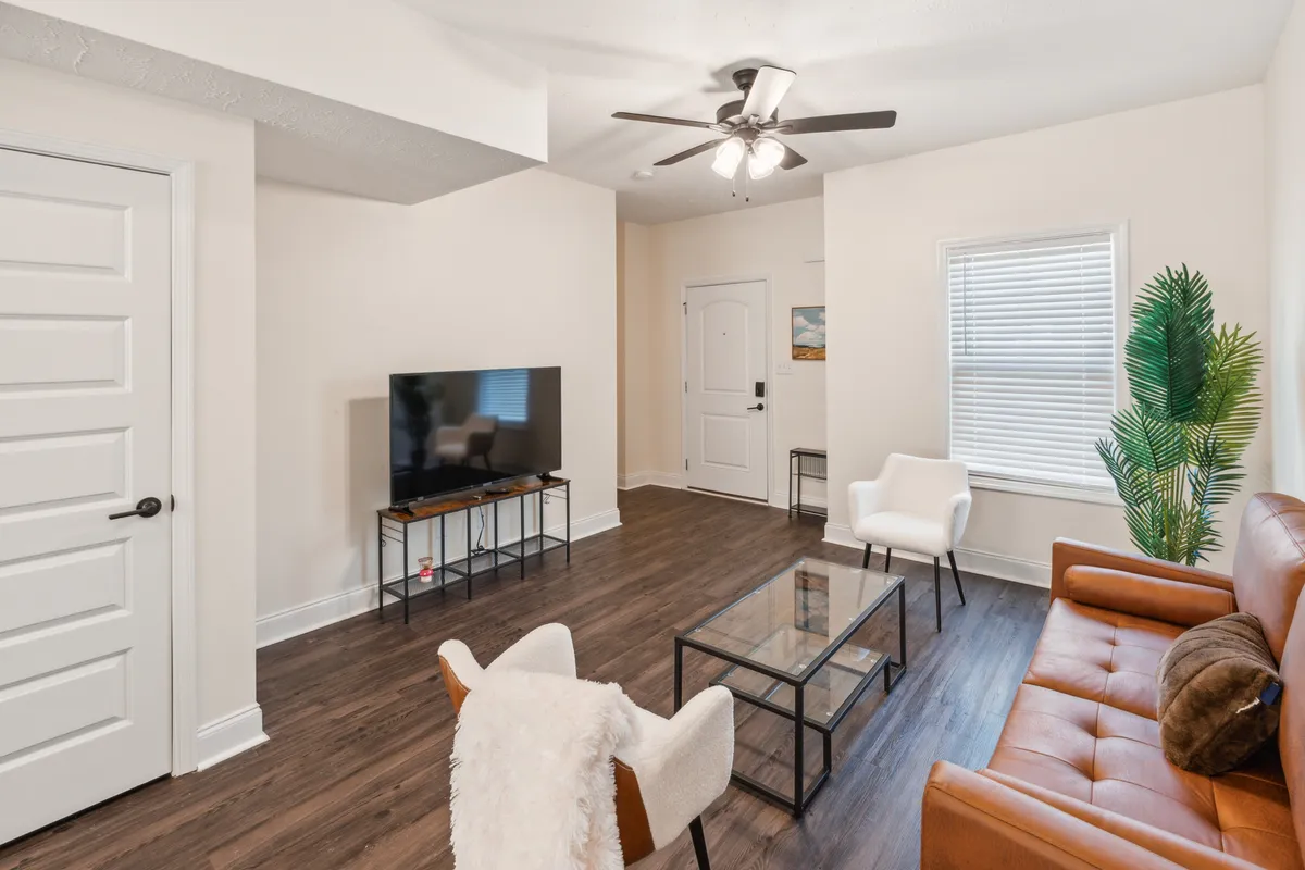 A welcoming living room with a brown leather sofa, glass coffee table, TV on a stand, potted plant, and white chairs. The scene is set for relaxing, unwinding, and spending quality time together after a day of adventure.