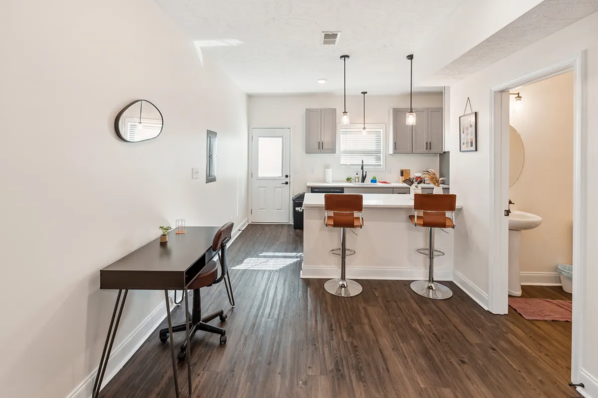 This interior scene centers on a multifunctional kitchen island with bar stools and a dedicated desk space. The area is bright, cozy, and designed for both work and socializing—ideal for focused work hours or relaxed meals at home.