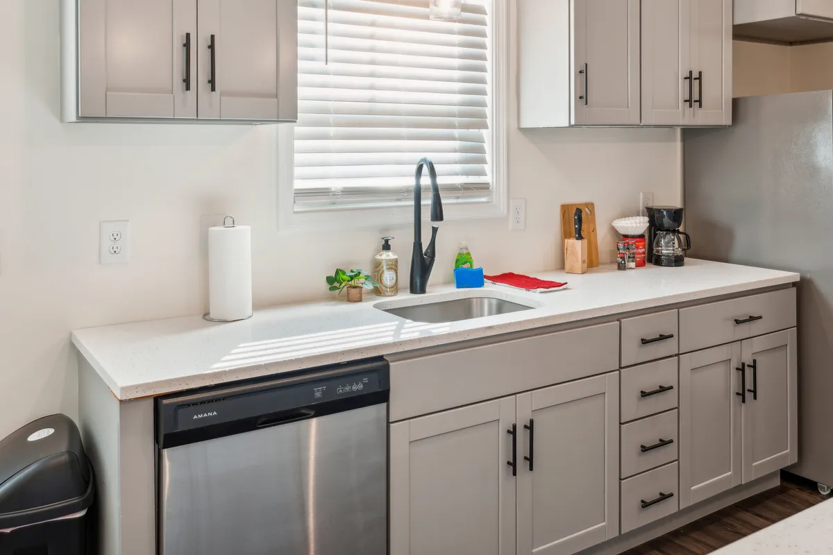 A close-up view of the kitchen’s practical features, including a modern sink with a sleek faucet, a built-in dishwasher, and countertop essentials like a coffee maker and cutting board. The scene suggests readiness for cooking and easy clean-up, highlighting the kitchen’s functionality and attention to detail.