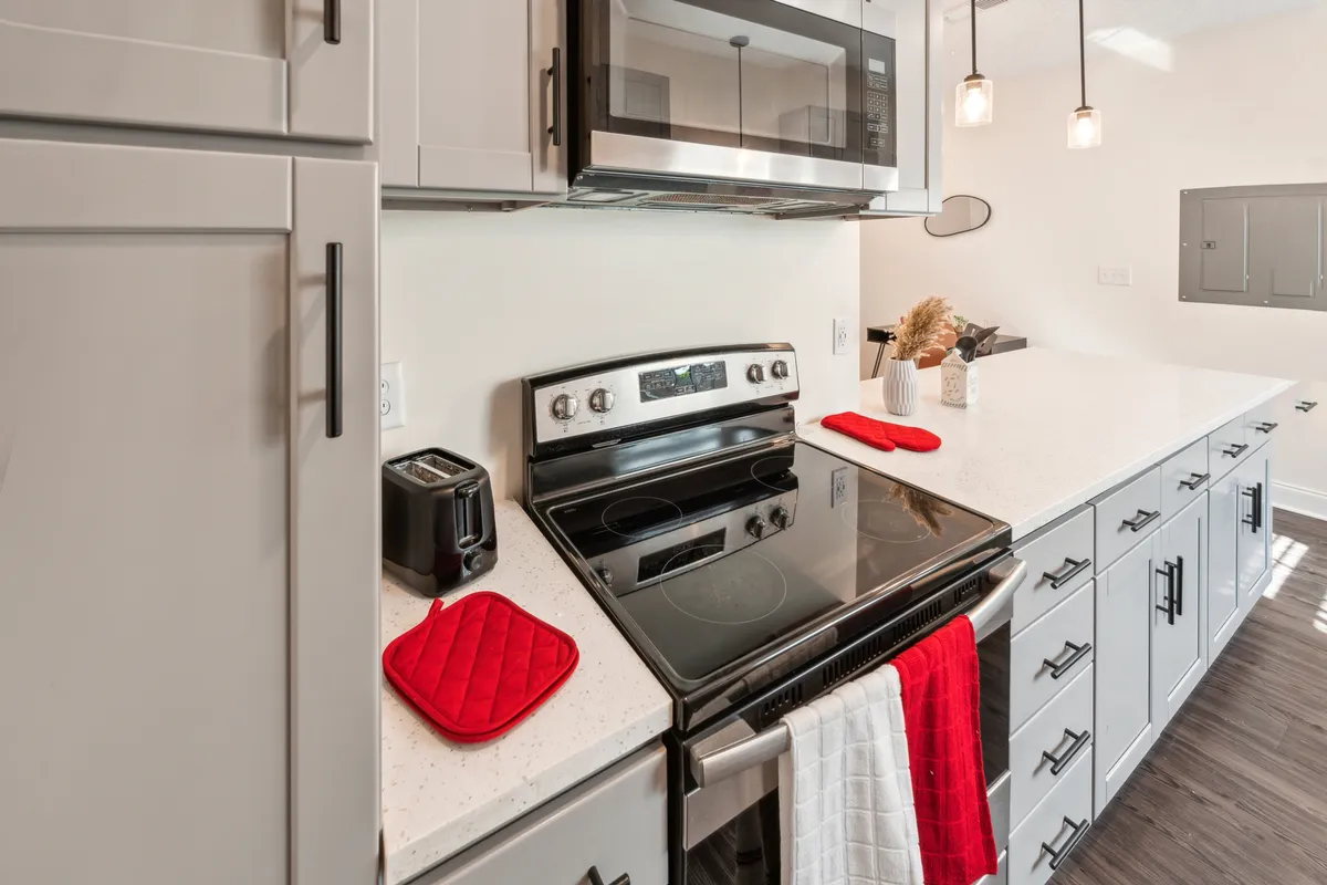 A view of a modern kitchen featuring a stainless steel stove, a gleaming white countertop, and vibrant red kitchen accessories. The space feels inviting and is set up for cooking, socializing, and entertaining, hinting at the convenience of preparing meals in your new temporary home.