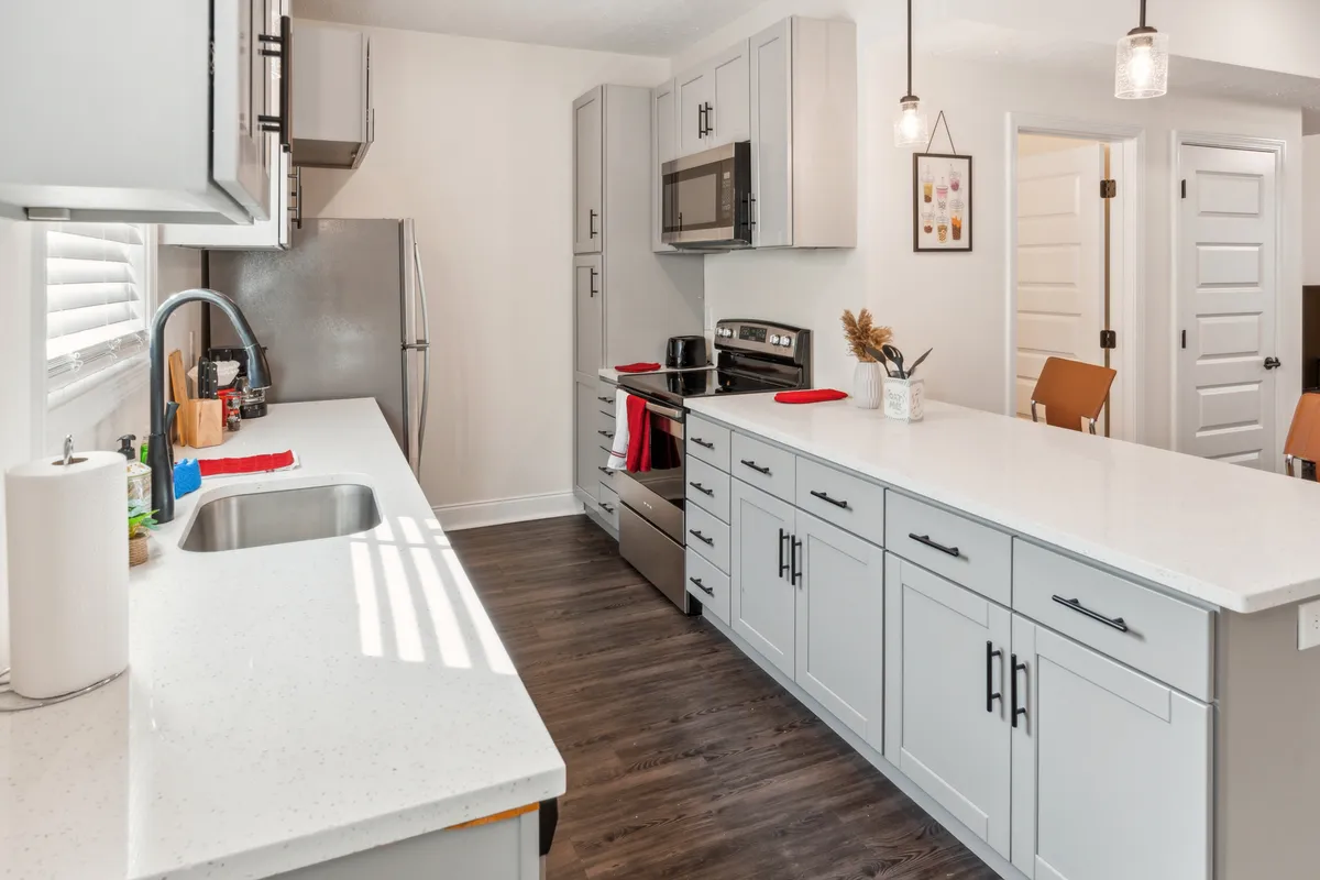 Another perspective of the kitchen, this time highlighting the island, stainless steel appliances, a large sink with a stylish faucet, and ample cabinetry. The clean lines and modern finishes reinforce the idea of a space that is both practical for meal prep and inviting for socializing or family time.